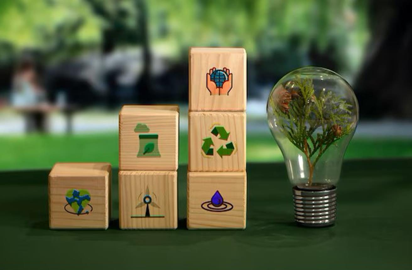 Sustainability icons on wooden blocks beside a light bulb with a plant